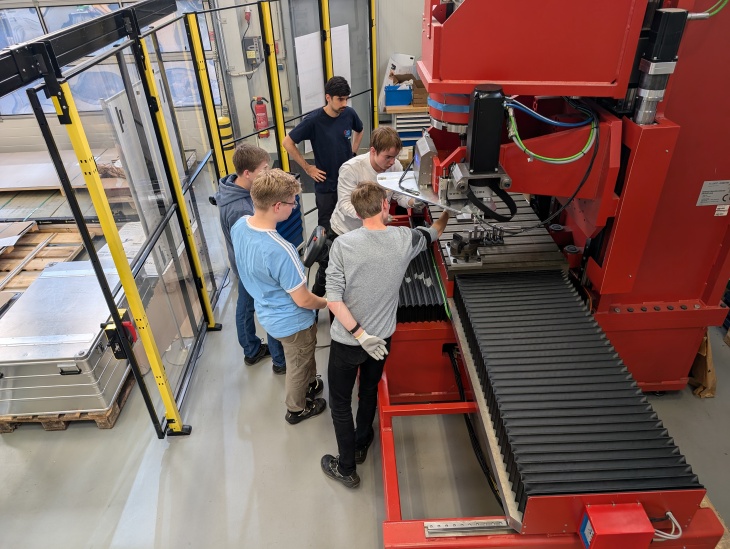 Der Werkstoffwissenschafler Lucas Salomao de Oliveira bereitet gemeinsam mit den Schülern an der Reibauftragschweißmaschine bei WDS eine Aluminium-Mehrschicht-Reibauftragschweißung vor. Foto: Hereon/Arne Roos Jugendliche bei den Werkstoffferien am Hereon.